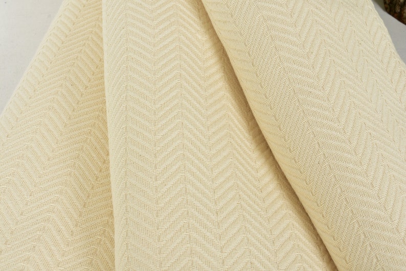 May include: Cream-colored fabric with a subtle herringbone pattern. The fabric is folded in thirds, showing the texture and weave.