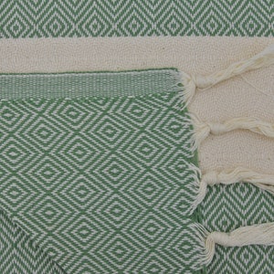 May include: A green and white patterned Turkish towel with fringe tassels. The towel is folded in half and the fringe is visible on the right side of the image.