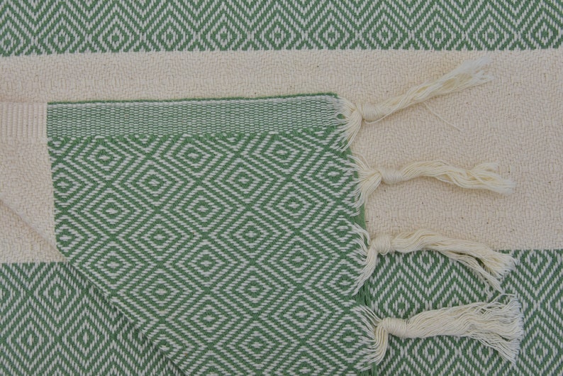 May include: A green and white patterned Turkish towel with fringe tassels. The towel is folded in half and the fringe is visible on the right side of the image.
