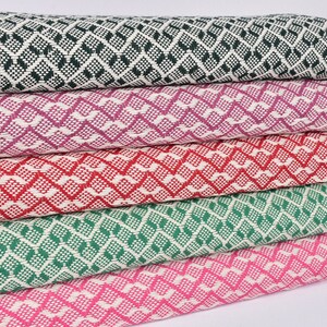 May include: Five woven blankets stacked on top of each other. The blankets are in a variety of colours, including green, pink, red, and purple. The blankets have a diamond pattern and are made of a soft, comfortable material.