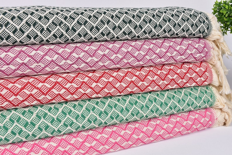 May include: Five woven blankets stacked on top of each other. The blankets are in a variety of colours, including green, pink, red, and purple. The blankets have a diamond pattern and are made of a soft, comfortable material.