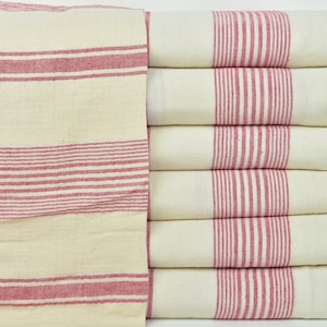 May include: A stack of eight white towels with red stripes. The towels have a fringed edge and are folded neatly.