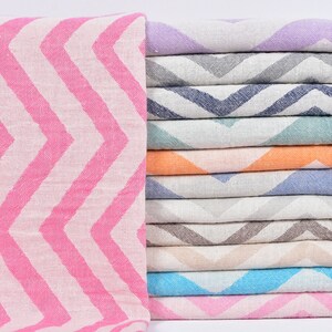 Puede incluir: Una pila de 12 toallas coloridas con un patrón de chevron. Las toallas están hechas de algodón y tienen flecos en los extremos. Las toallas son de varios colores, incluyendo rosa, morado, gris, azul, verde, naranja y beige.