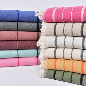 May include: A stack of striped towels in various colors, including pink, blue, gray, beige, and green. The towels are folded and arranged in a neat pile.
