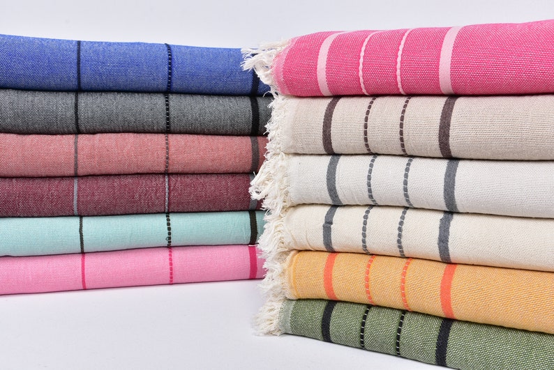 May include: A stack of striped towels in various colors, including pink, blue, gray, beige, and green. The towels are folded and arranged in a neat pile.