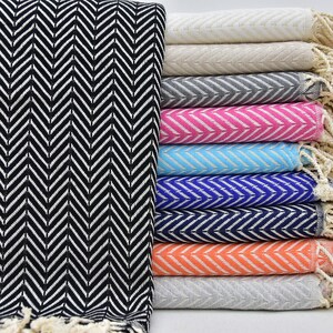 May include: A stack of ten towels with a chevron pattern in various colors, including black, white, gray, pink, blue, and orange. The towels have fringe on the ends.
