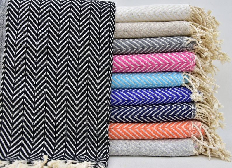 May include: A stack of ten towels with a chevron pattern in various colors, including black, white, gray, pink, blue, and orange. The towels have fringe on the ends.