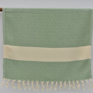 May include: A green and white patterned Turkish towel with fringe. The towel has a diamond pattern and a white stripe.