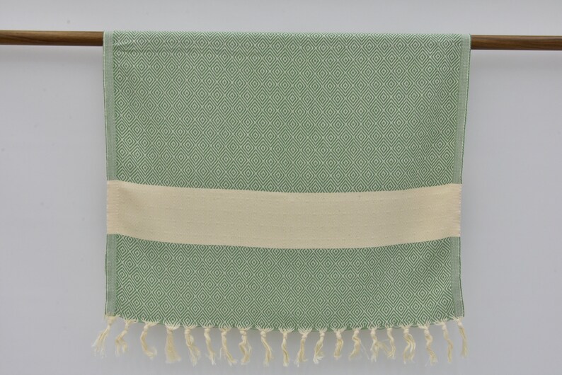 May include: A green and white patterned Turkish towel with fringe. The towel has a diamond pattern and a white stripe.