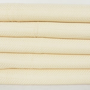 May include: A stack of four cream-colored woven blankets with a herringbone pattern.