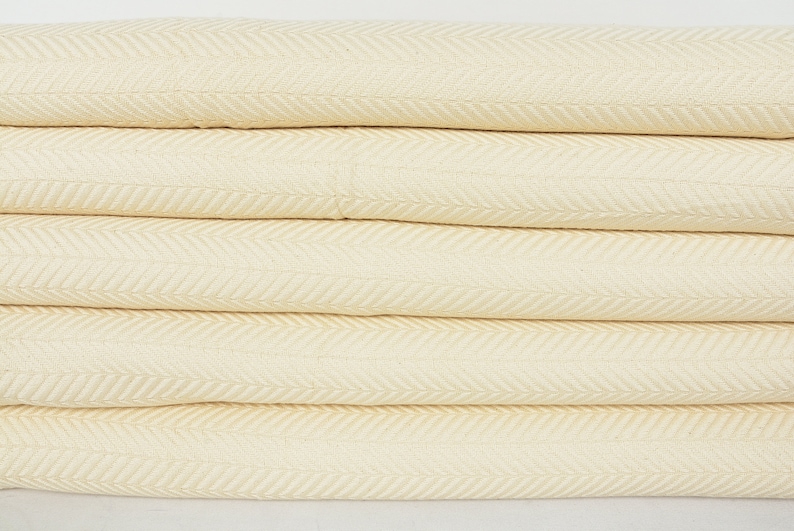 May include: A stack of four cream-colored woven blankets with a herringbone pattern.