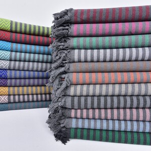 May include: A stack of colorful striped towels with fringe edges. The towels are folded and arranged in a row. The towels are made of cotton and have a soft, absorbent texture.