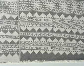 Peut inclure: Une couverture en tissu gris et blanc à motifs avec une bordure frangée. La couverture présente un motif géométrique avec des motifs répétitifs.