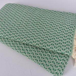 May include: A green and white patterned throw blanket with fringe. The blanket is folded in half and has a diamond pattern.