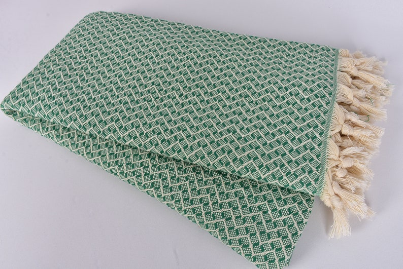 May include: A green and white patterned throw blanket with fringe. The blanket is folded in half and has a diamond pattern.