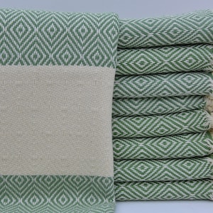 May include: A stack of green and white patterned Turkish towels with fringe. The towels are folded and stacked on a white surface.