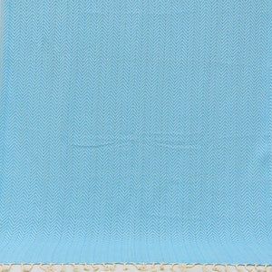 May include: A light blue beach towel with a white chevron pattern. The towel has a fringe border.
