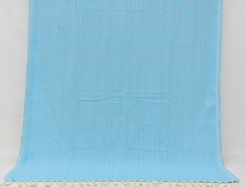 May include: A light blue beach towel with a white chevron pattern. The towel has a fringe border.