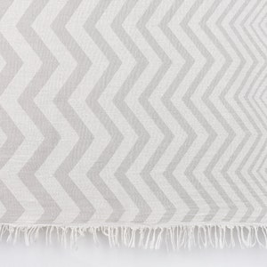 May include: A gray and white chevron patterned throw blanket with a fringe border.