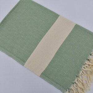 May include: A green and white patterned Turkish towel with fringe. The towel has a diamond pattern and a white stripe down the center.