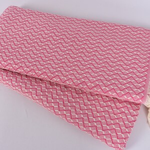 May include: Pink and white patterned throw blanket with a fringe border. The blanket is folded in half and the fringe is visible on the right side.