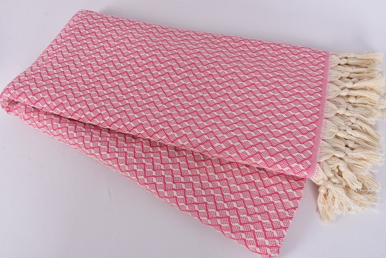May include: Pink and white patterned throw blanket with a fringe border. The blanket is folded in half and the fringe is visible on the right side.
