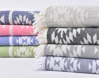 May include: A stack of six patterned Turkish towels in various colors, including gray, pink, blue, green, and white. The towels have a geometric design and fringe edges.