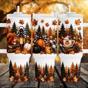 May include: A white tumbler with a handle and straw featuring an autumn-themed wrap design. The print displays a squirrel, a lantern, pumpkins, a mug with whipped cream, pine trees, and falling orange leaves against a forest background.