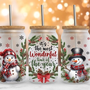 May include: Three glass tumblers with lids and straws, featuring a winter holiday theme. Each tumbler has a different design: one with a snowman wearing a red and black plaid scarf, one with a snowman wearing a black top hat, and one with a wreath with the text "it's the most Wonderful time of the year".
