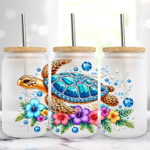 Puede incluir: Tres vasos de vidrio esmerilado con tapas de bambú y pajitas de metal. Cada vaso presenta un diseño de tortuga marina colorida con gemas azules, rodeado de flores tropicales en tonos rosa, azul y amarillo.