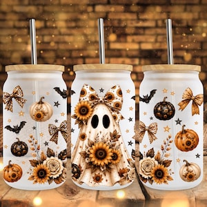 Op de afbeelding: Drie matglazen bekers met bamboe deksels en metalen rietjes, voorzien van een herhalend patroon van spoken, zonnebloemen, pompoenen, strikken met luipaardprint, vleermuizen en sterren in tinten oranje, bruin, zwart en crème.
