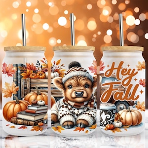 Puede incluir: Tres vasos de vidrio con tapas de madera y pajitas de metal. Cada vaso presenta un diseño de otoño con calabazas, hojas y un ternero con gorro y suéter. Un vaso dice "Hey Fall".