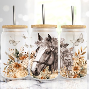May include: Three glass tumblers with bamboo lids and metal straws. Each tumbler features a different design with a watercolor-style illustration of a horse's head, flowers, and butterflies in shades of brown, beige, and white.