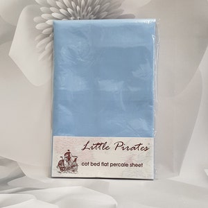 May include: A baby blue cot bed flat percale sheet, sealed in clear plastic. The label reads "Little Pirates" and features a pirate ship illustration. The sheet is designed for a cot bed.