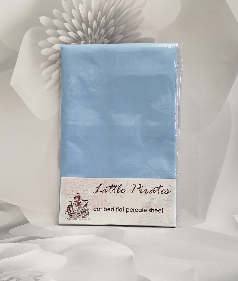 May include: A baby blue cot bed flat percale sheet, sealed in clear plastic. The label reads "Little Pirates" and features a pirate ship illustration. The sheet is designed for a cot bed.