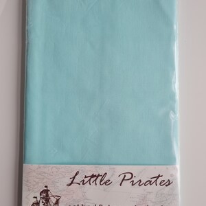 May include: A flat cot bed sheet in a pale turquoise hue, sealed in transparent packaging. The label reads "Little Pirates" and "cot bed flat percale sheet", accompanied by a ship illustration.