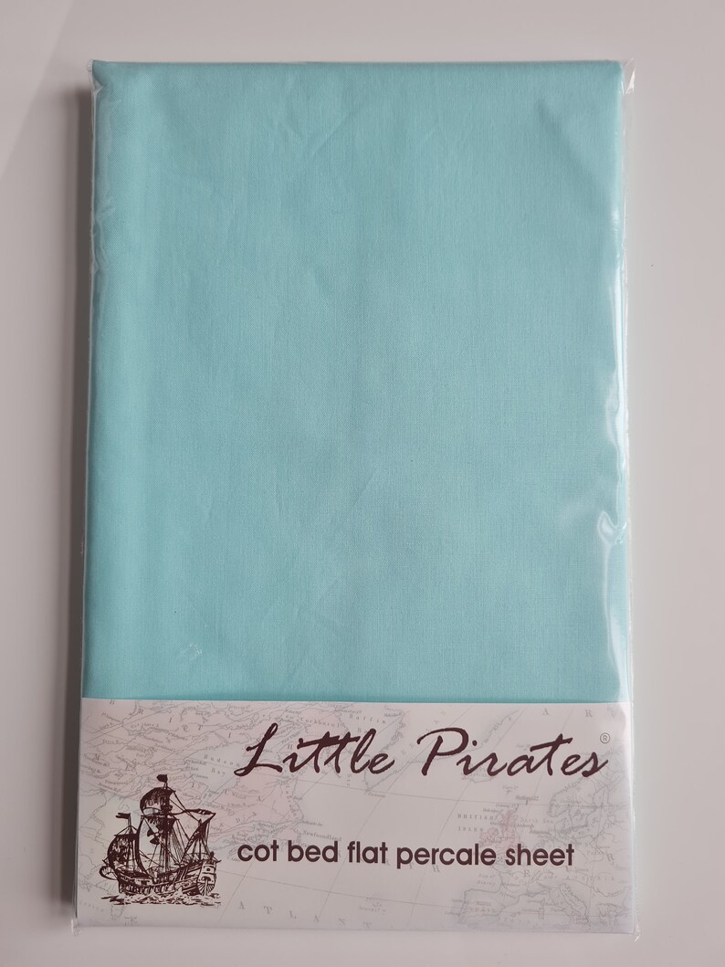 May include: A flat cot bed sheet in a pale turquoise hue, sealed in transparent packaging. The label reads "Little Pirates" and "cot bed flat percale sheet", accompanied by a ship illustration.