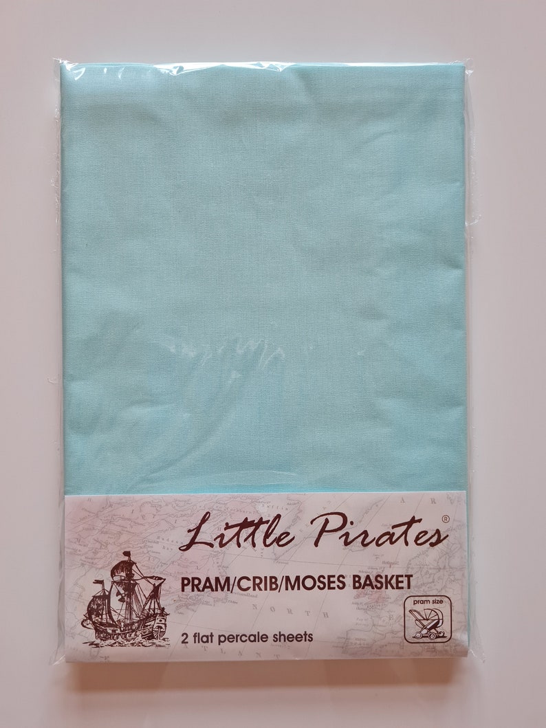May include: A package of two flat percale sheets in a light blue color, designed for a pram, crib, or Moses basket. The packaging features the "Little Pirates" logo, a map design, and a graphic of a pram.