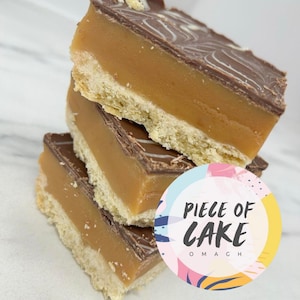 Peut inclure: Des tranches de shortbread au caramel empilées, avec une base biscuitée, une couche de caramel et une garniture au chocolat avec un tourbillon blanc. Un autocollant coloré avec le texte "PIECE OF CAKE OMAGH" est au premier plan.
