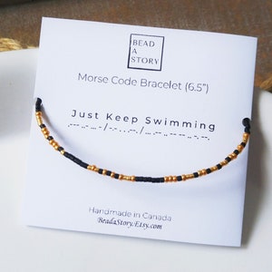 May include: A black and gold beaded bracelet with the message "Just Keep Swimming" in Morse code. The bracelet is 6.5 inches long and is handmade in Canada.