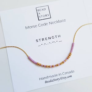 Peut inclure: Un collier délicat en chaîne dorée avec un message perlé en rose et or. Le message est "STRENGTH" en code Morse. La carte indique "Bead a Story Collier en code Morse Fait à la main au Canada Beadastory.Etsy.com"
