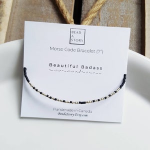 May include: A black and silver beaded bracelet with the words "Beautiful Badass" in Morse code on a white card. The card also says "Morse Code Bracelet (7")" and "Handmade in Canada BeadaStory.Etsy.com".