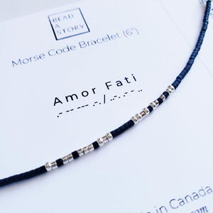 May include: A black and silver beaded bracelet with the text "Amor Fati" and the Morse code translation below. The bracelet is 15 cm long and is labelled "Morse Code Bracelet (6")".