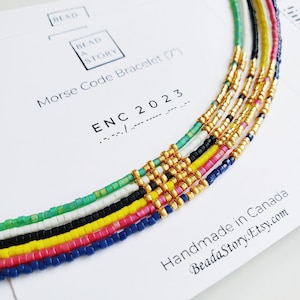 May include: Multicoloured beaded bracelet with gold beads, featuring the text "Morse Code Bracelet (7)" and "ENC 2023" in black text on a white background.