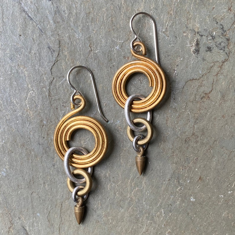 Pode incluir: Brincos de ouro e prata com um design em espiral e v&aacute;rios an&eacute;is conectados. Os brincos t&ecirc;m uma ponta pontiaguda na parte inferior.