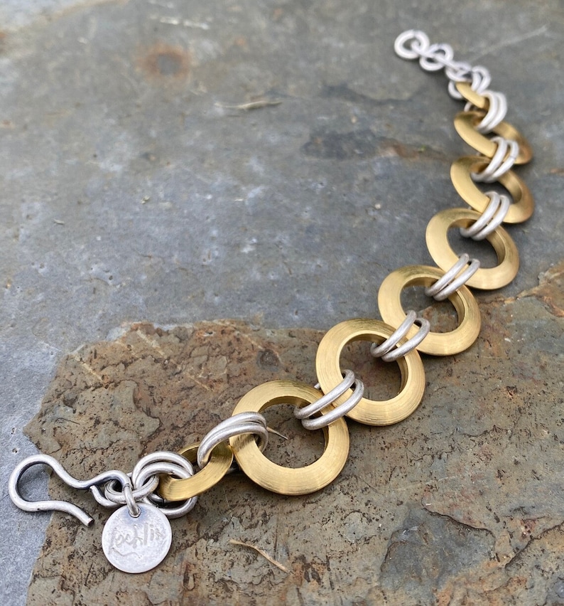 May include: A gold and silver bracelet with a hook clasp. The bracelet is made of interlocking circles.