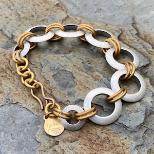 May include: A silver and gold bracelet with a chain link closure and a round, interlocking design. The bracelet has a small tag with the word "Rockhill" on it.
