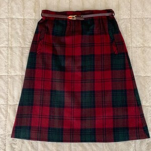 May include: A red and green plaid skirt with a brown leather belt. The skirt has two pockets on the sides.