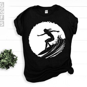 May include: Black t-shirt with a white silhouette of a person surfing on a wave.