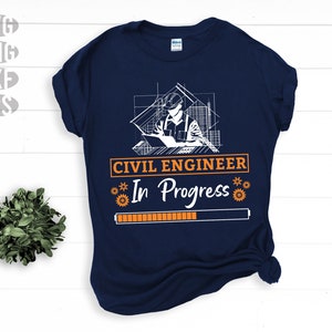 May include: Navy blue t-shirt with a white and orange graphic. The graphic features a civil engineer with blueprints, the text "CIVIL ENGINEER In Progress", and a loading bar. The shirt also has SVG, PNG, DXF, and EPS file type icons.